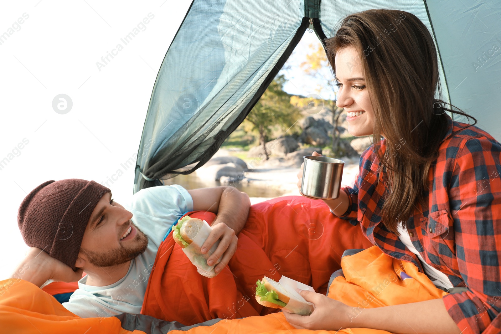 Photo of Young couple having breakfast in sleeping bags inside of camping tent