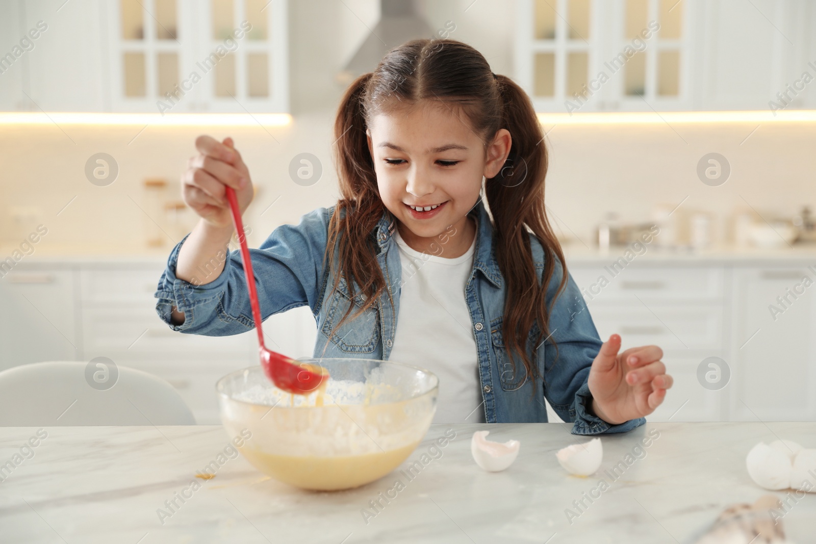 Photo of Cute little girl cooking dough at table in kitchen