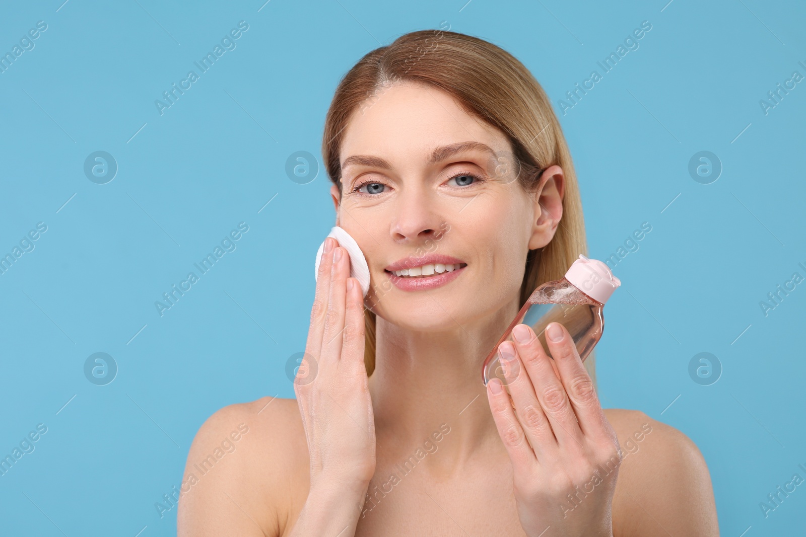 Photo of Beautiful woman removing makeup with cotton pad on light blue background