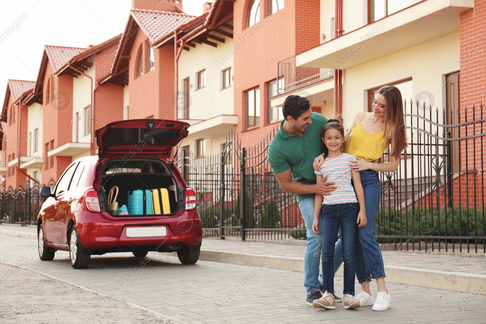 Photo of Happy parents hugging their daughter near family car on street