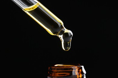 Photo of Dripping tincture from pipette into bottle on black background, closeup