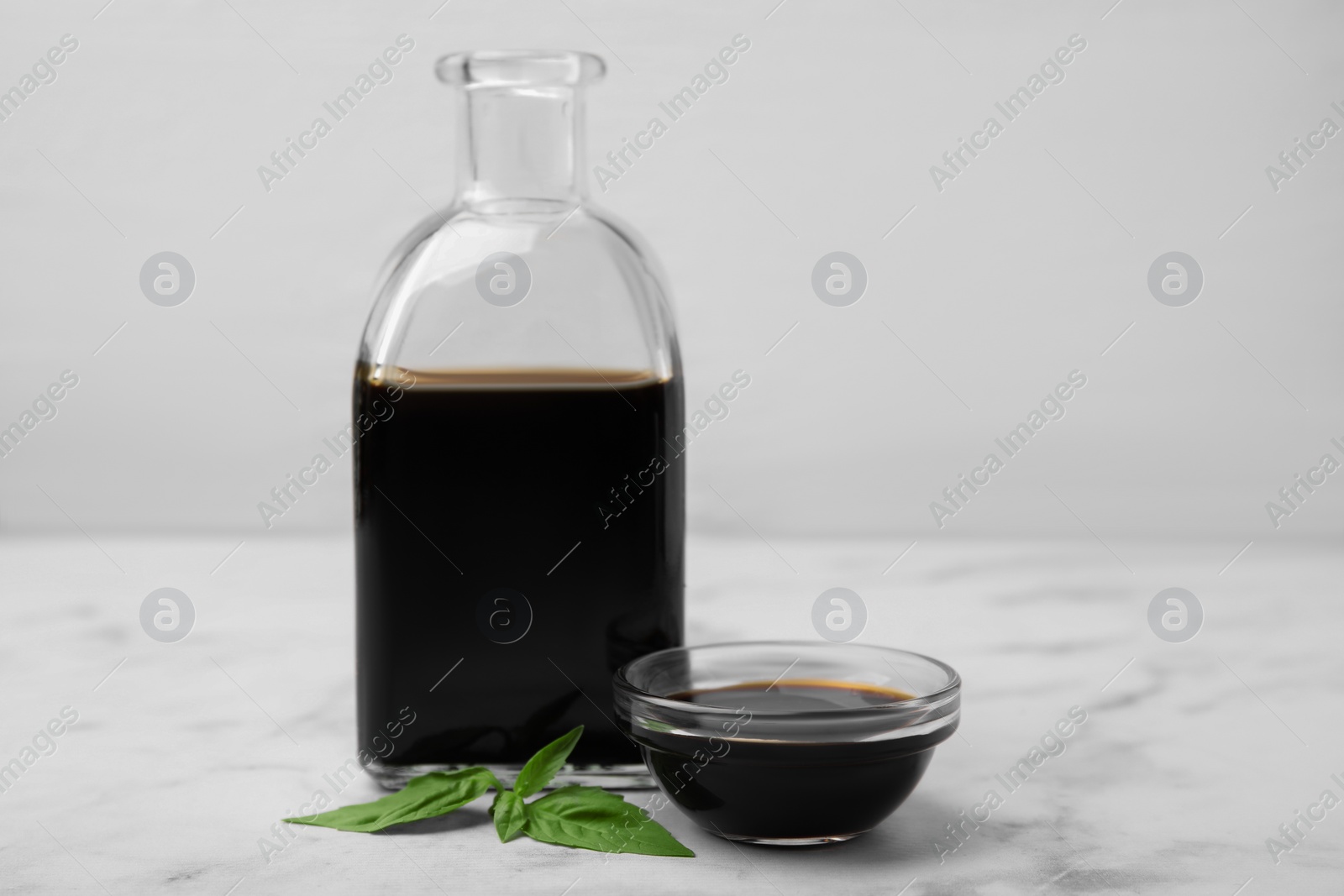 Photo of Organic balsamic vinegar and basil on white marble table