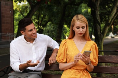 Photo of Young woman with smartphone ignoring her boyfriend in park. Boring date