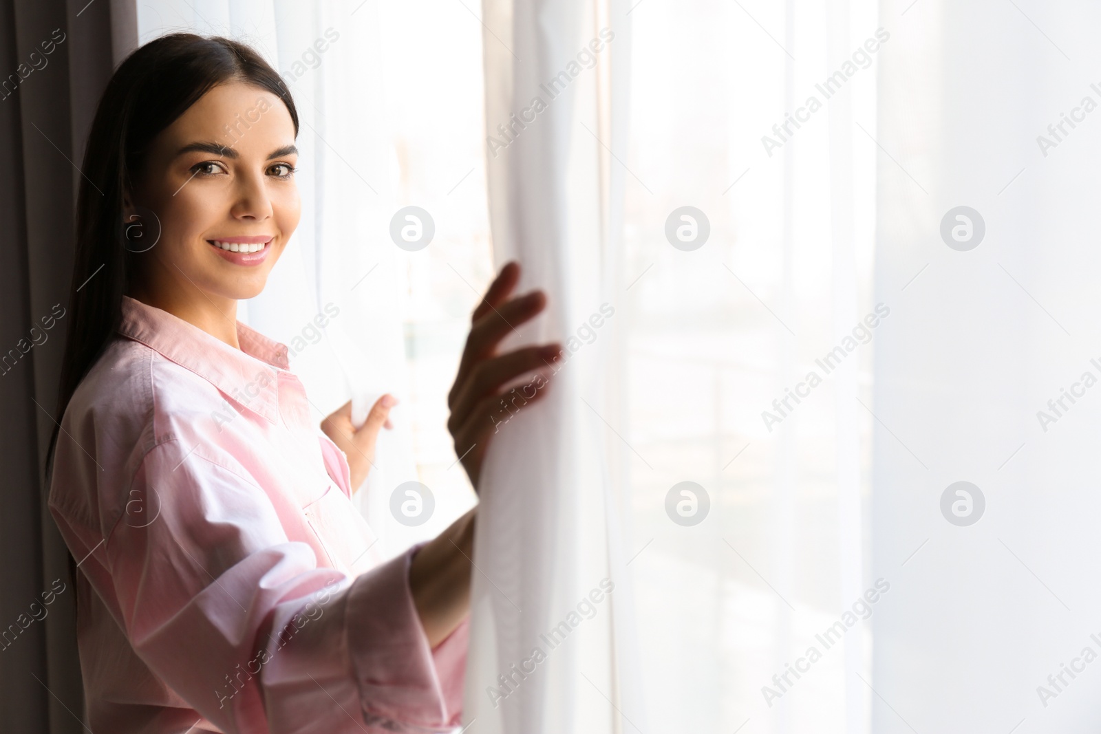 Photo of Woman opening window curtains at home in morning. Space for text