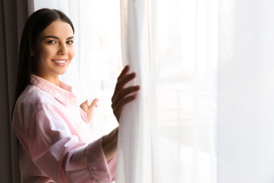 Woman opening window curtains at home in morning. Space for text