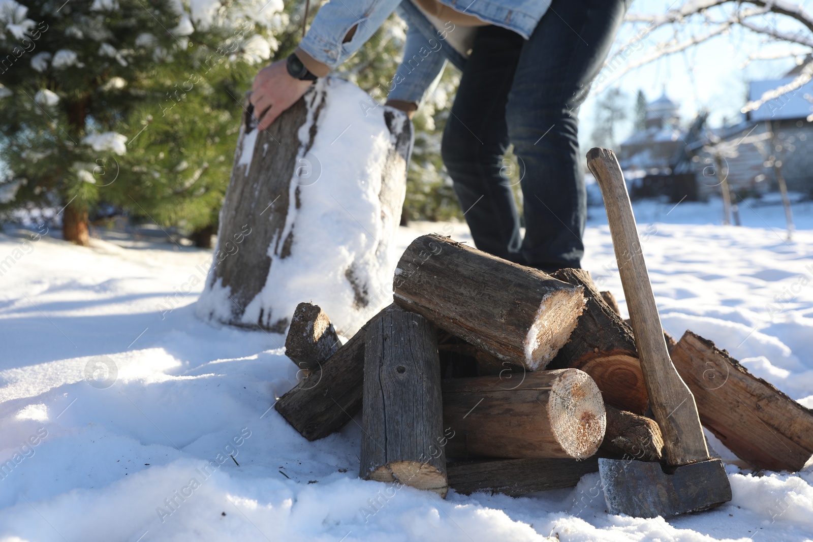 Photo of Man preparing stump for chopping outdoors, closeup. Axe and pile of logs on snow, selective focus