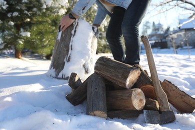 Man preparing stump for chopping outdoors, closeup. Axe and pile of logs on snow, selective focus