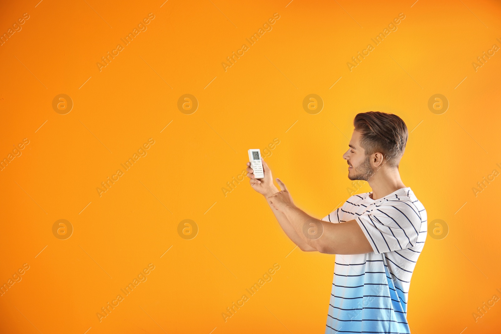 Photo of Young man with air conditioner remote on color background