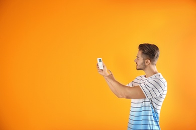 Young man with air conditioner remote on color background