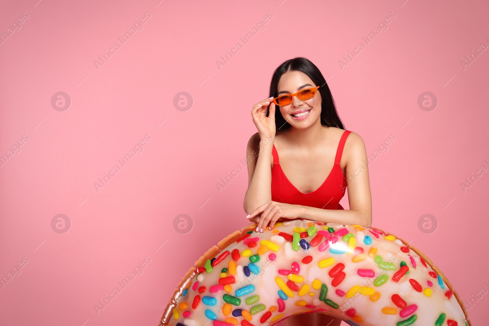 Photo of Young woman with stylish sunglasses holding inflatable ring against pink background. Space for text