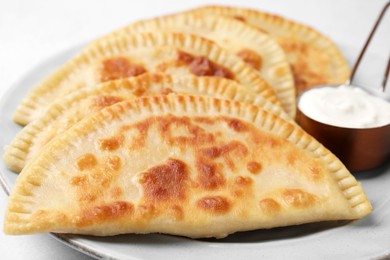 Photo of Delicious fried chebureki with cheese and sauce on light grey table, closeup