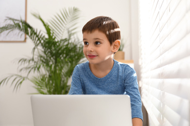 Happy little boy with modern laptop near window indoors