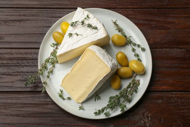 Photo of Plate with pieces of tasty camembert cheese, olives and rosemary on wooden table, top view