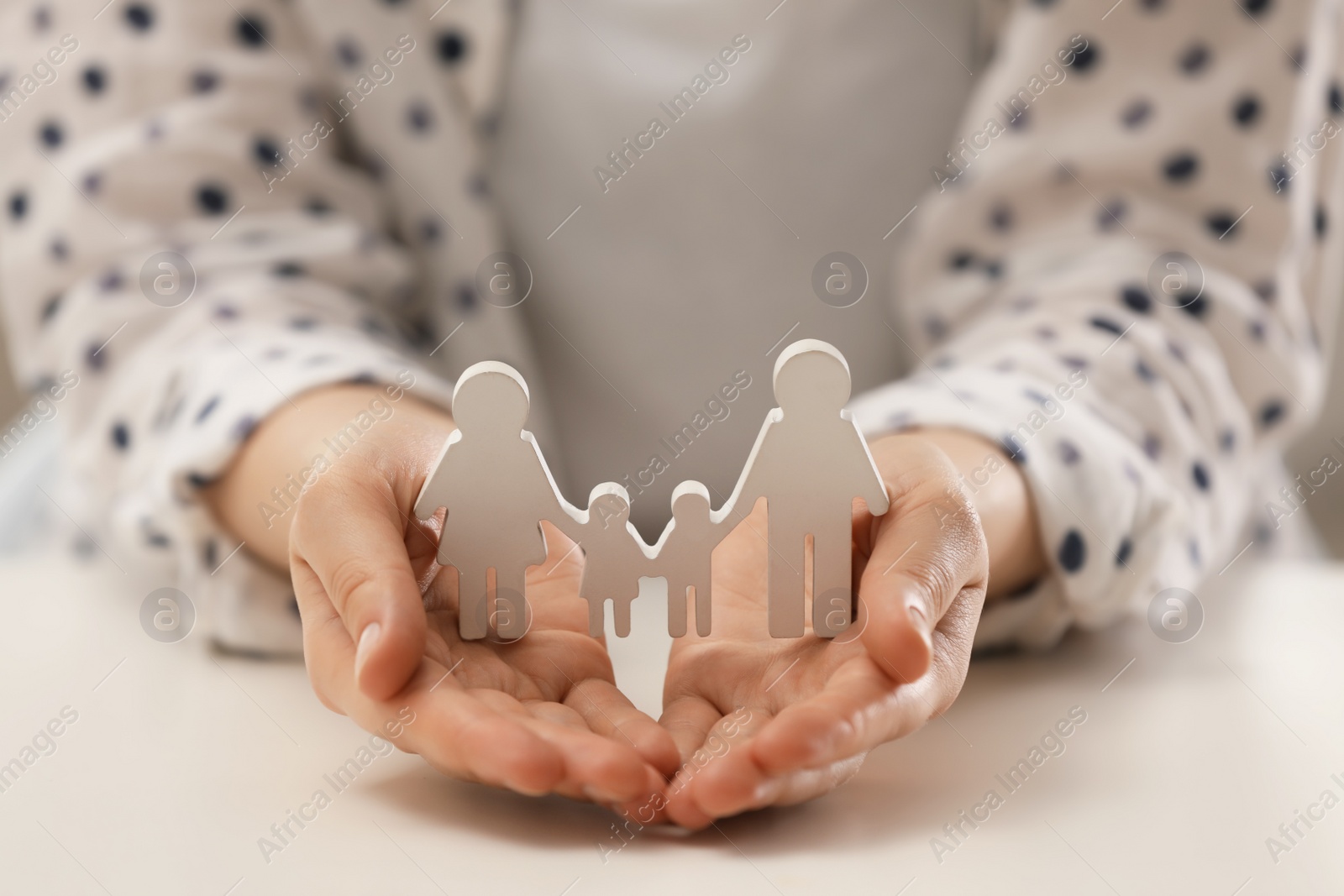 Photo of Woman holding figure of family at white table, closeup