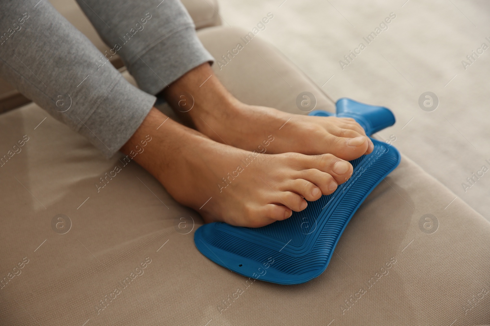 Photo of Man warming feet with hot water bottle on sofa, closeup