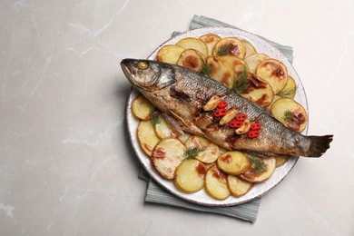 Photo of Plate with delicious baked sea bass fish and potatoes on light grey table, top view. Space for text
