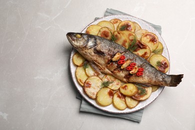 Plate with delicious baked sea bass fish and potatoes on light grey table, top view. Space for text