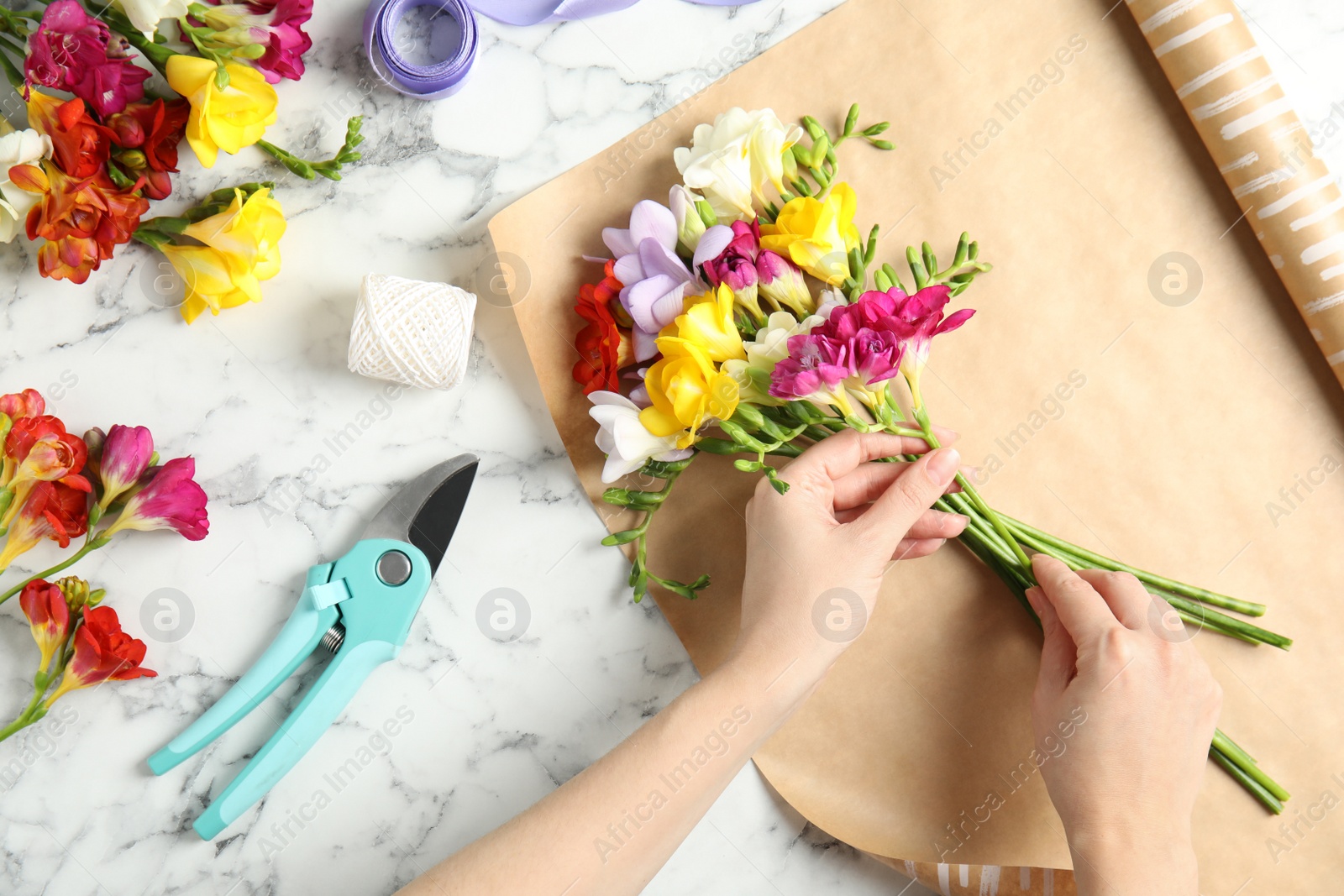 Photo of Woman making bouquet of freesia flowers at table, top view