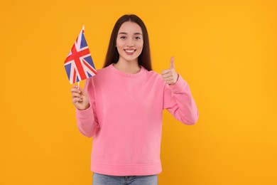 Photo of Young woman with flag of United Kingdom showing thumb up on orange background
