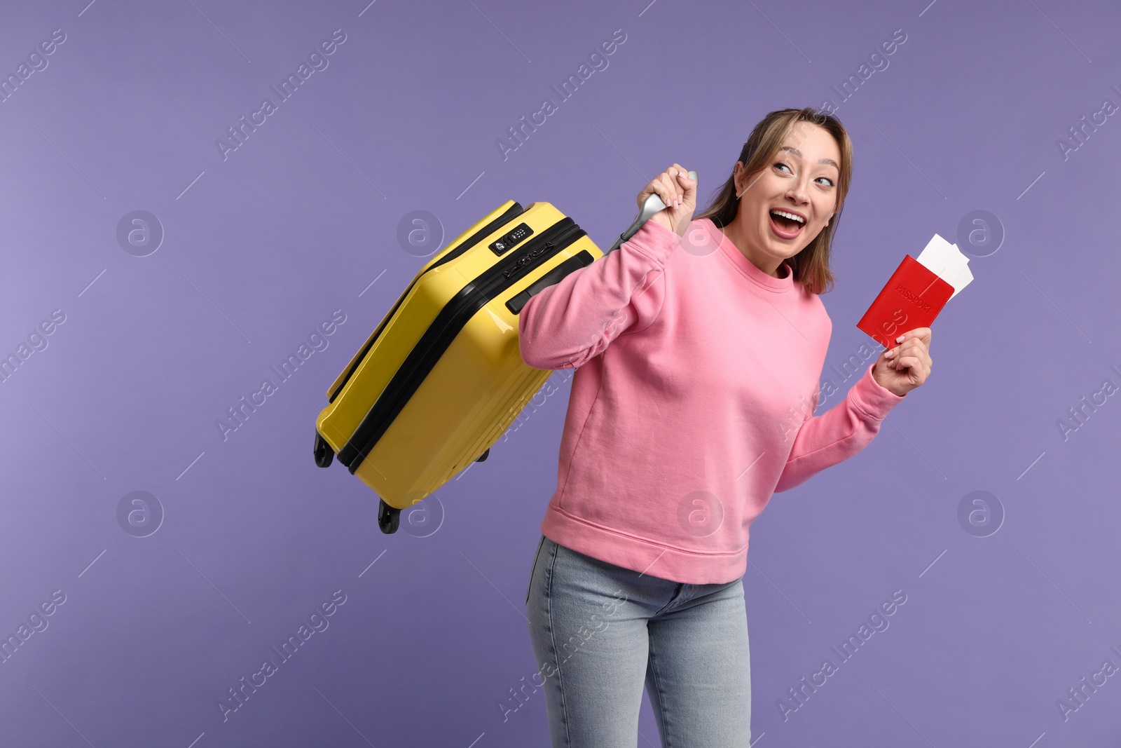 Photo of Emotional young woman with passport, ticket and suitcase on purple background, space for text