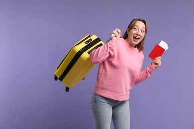 Emotional young woman with passport, ticket and suitcase on purple background, space for text