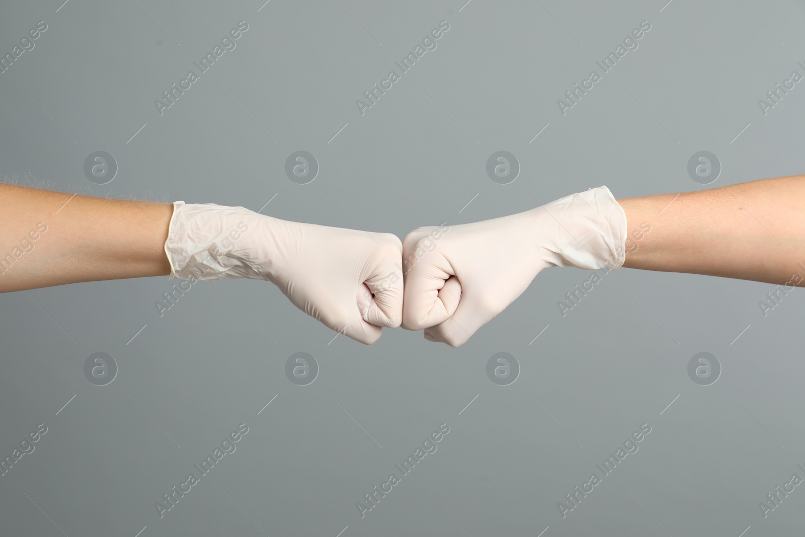 Photo of Doctors in medical gloves making fist bump on grey background, closeup