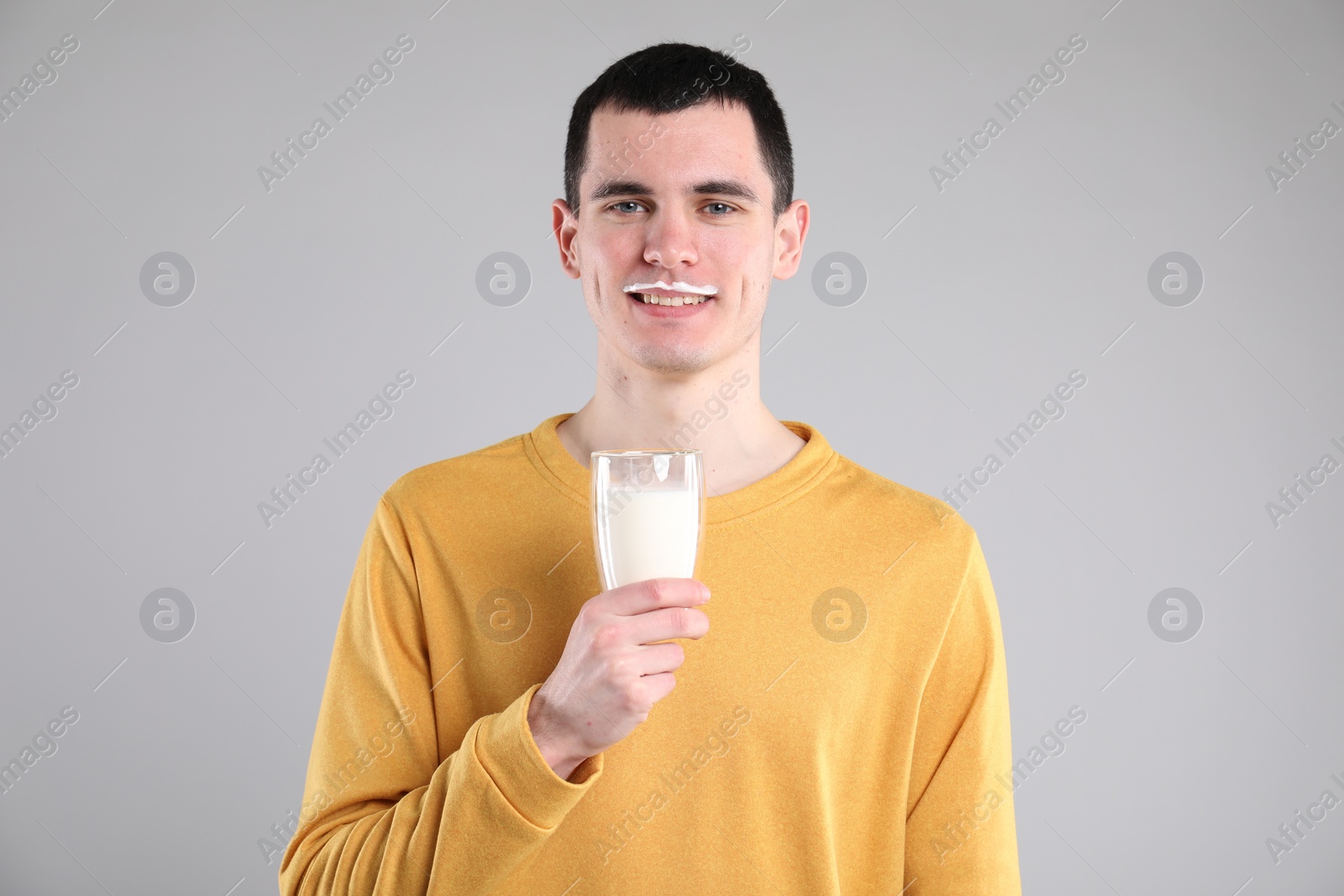 Photo of Happy man with milk mustache holding glass of tasty dairy drink on gray background