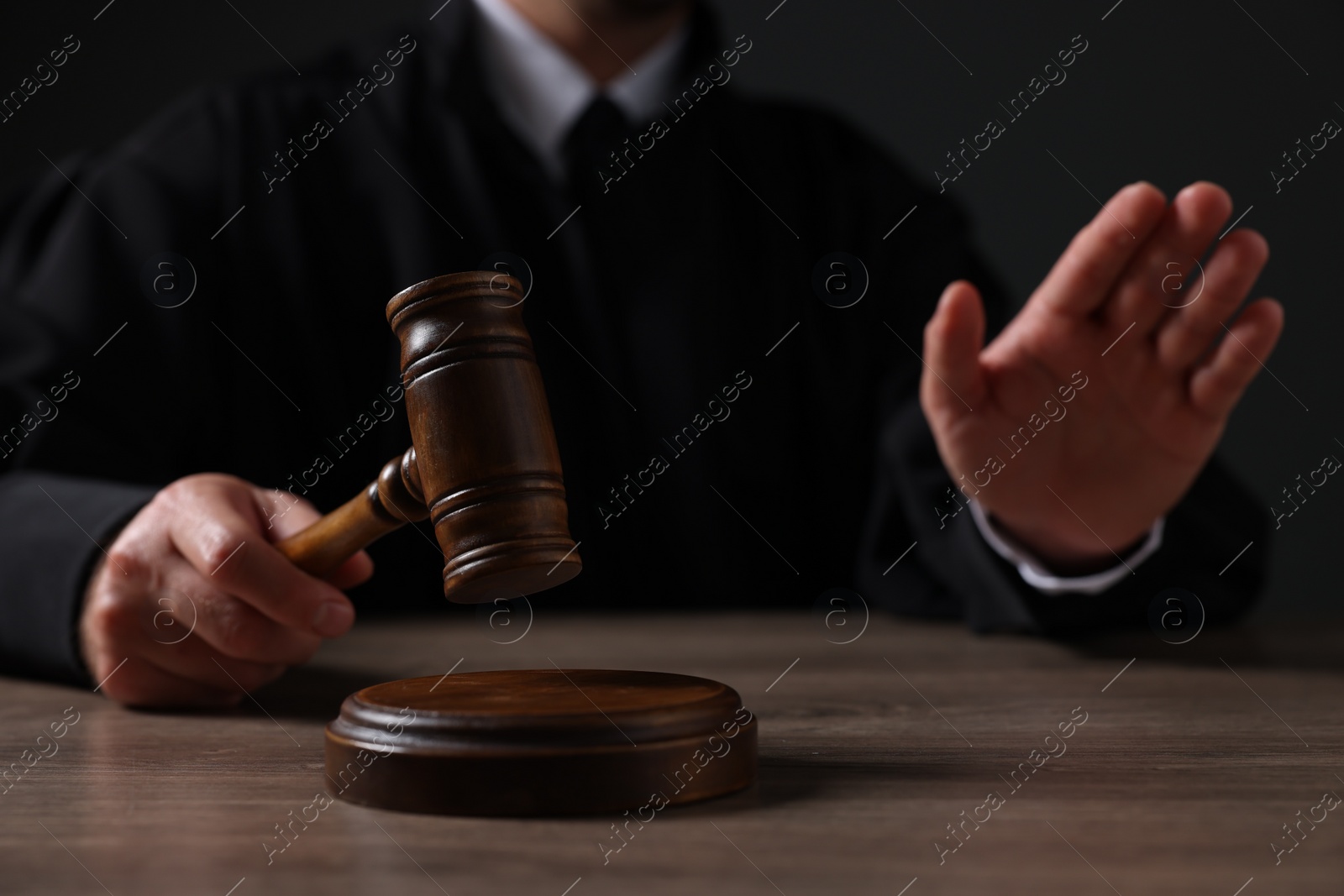 Photo of Judge with gavel showing stop gesture at wooden table against black background, closeup