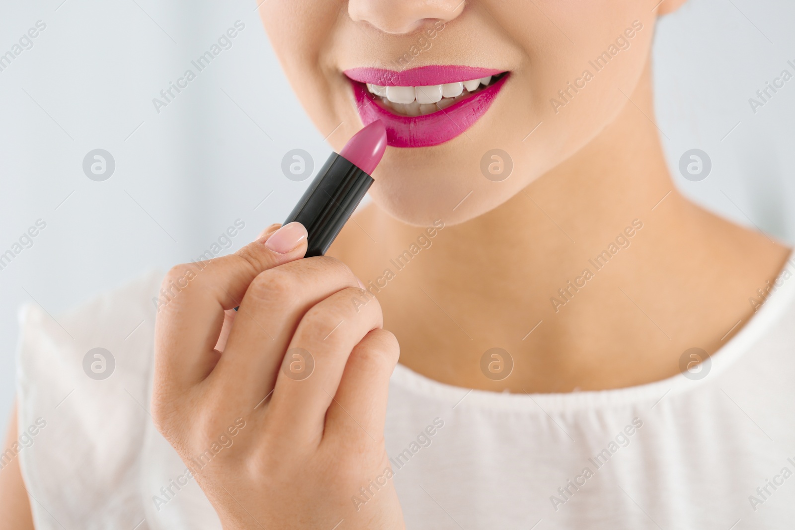 Photo of Beautiful woman applying lipstick on light background, closeup