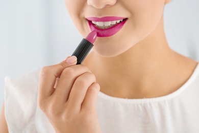 Beautiful woman applying lipstick on light background, closeup