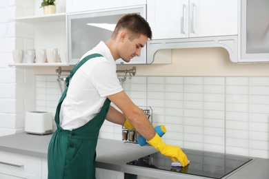 Male janitor cleaning kitchen stove with sponge in house