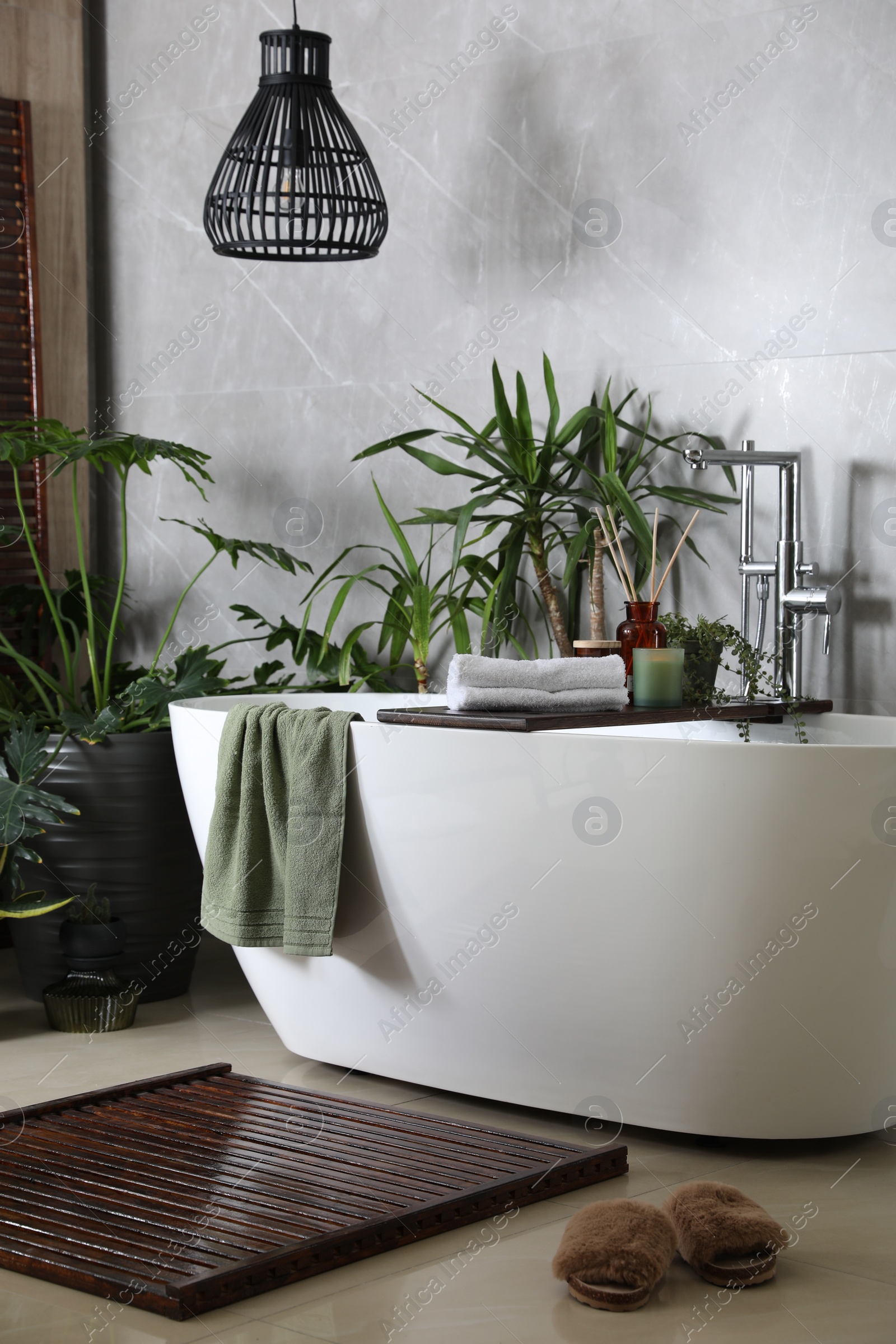 Photo of Modern white tub and beautiful green houseplants in bathroom. Interior design