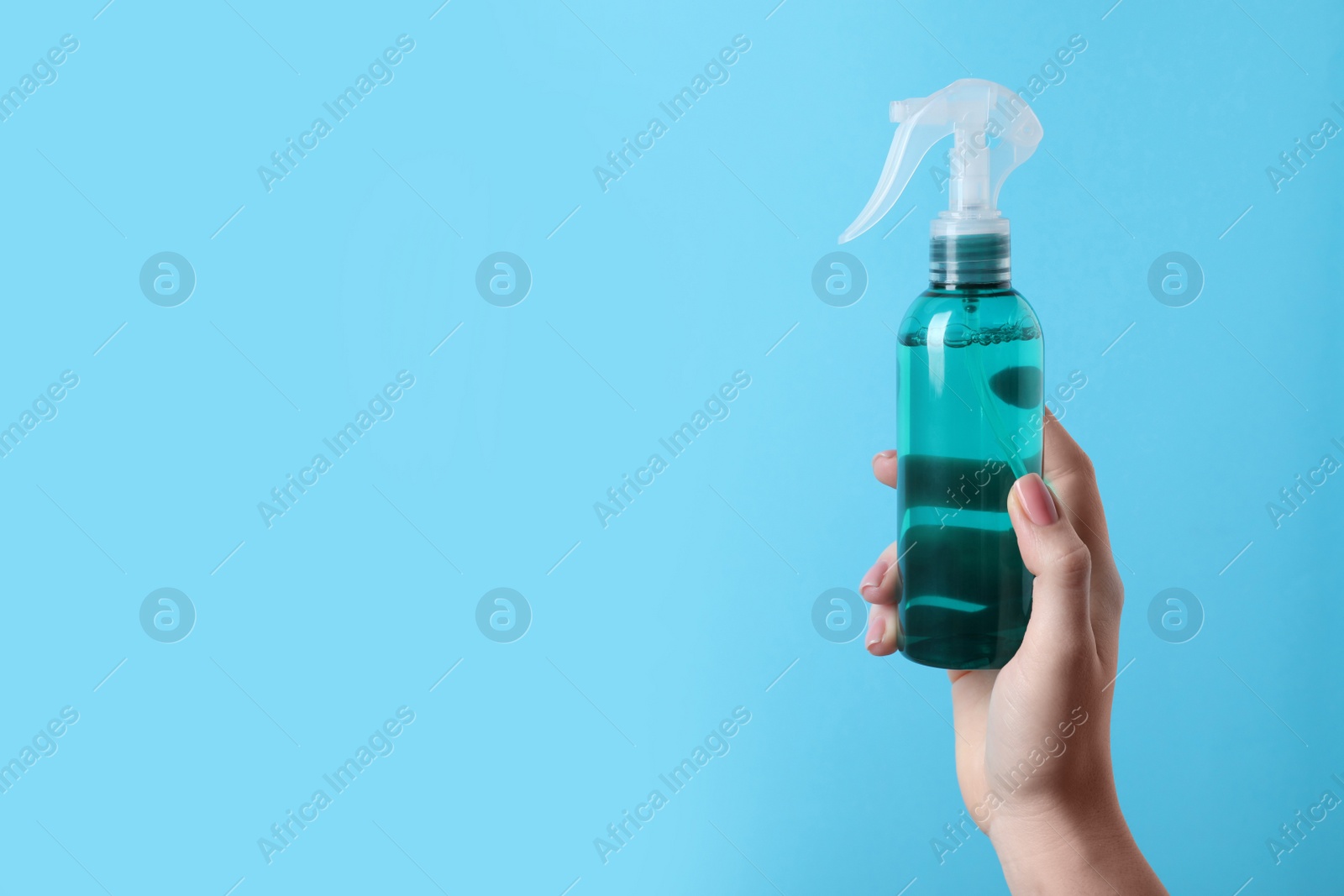 Photo of Woman holding spray bottle with thermal protection on light blue background, closeup. Space for text