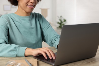 Photo of Young woman using laptop at wooden desk in room, closeup
