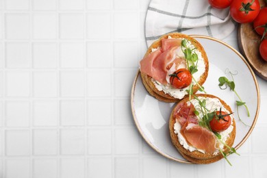 Photo of Tasty rusks with prosciutto, cream cheese and tomatoes served on white table, flat lay. Space for text