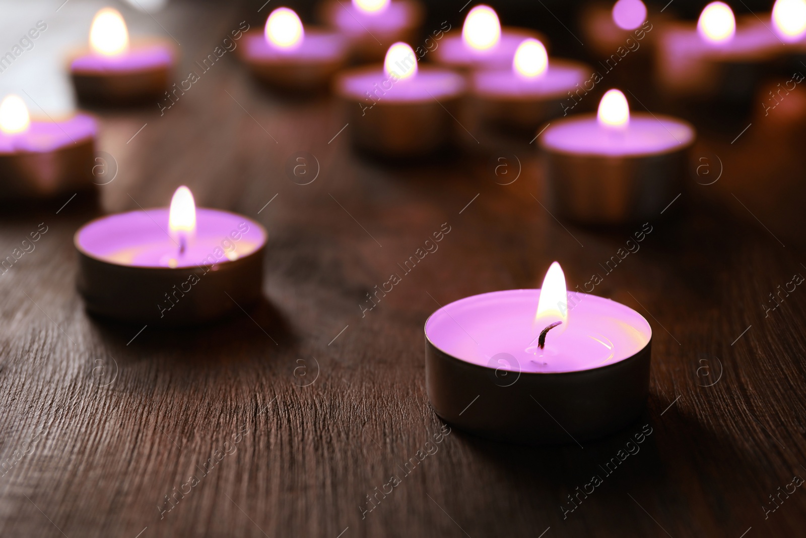 Image of Beautiful burning violet candles on wooden table, closeup. Funeral attributes