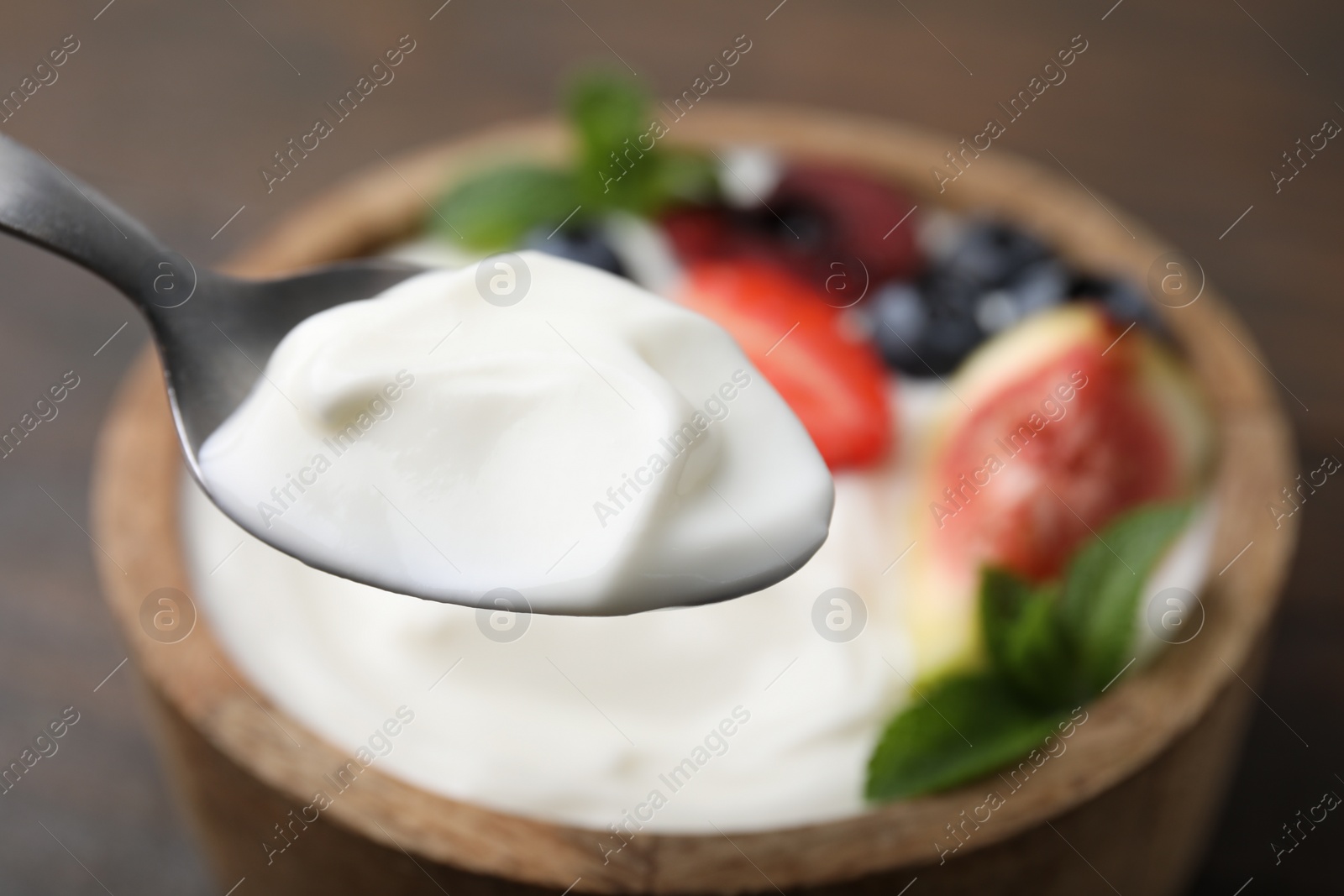 Photo of Spoon with tasty yogurt above bowl on table, closeup. Space for text