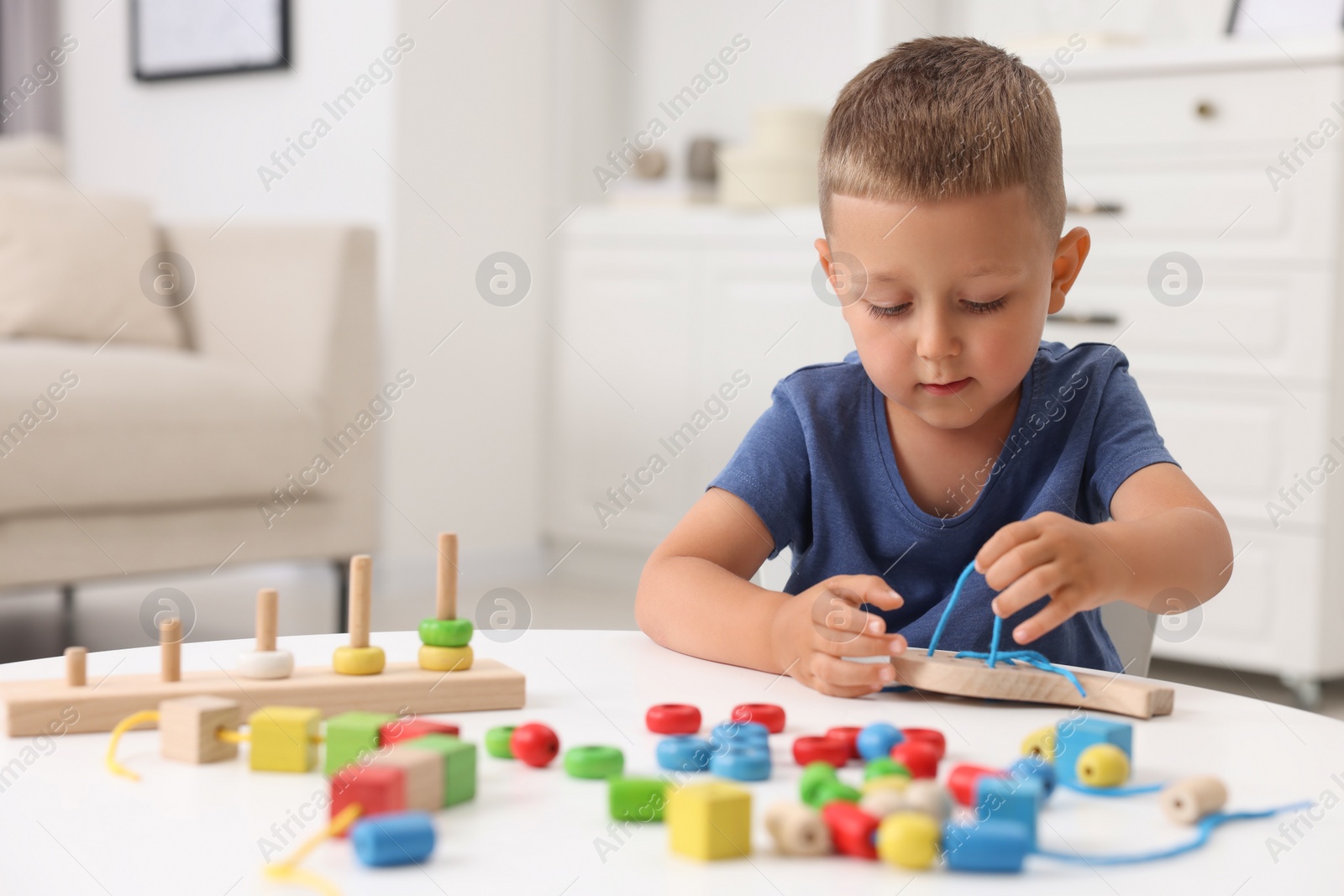 Photo of Motor skills development. Little boy playing with wooden lacing toy at white table indoors