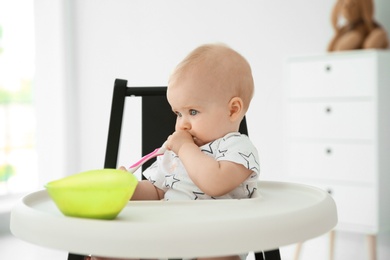 Cute little baby eating in high chair at home