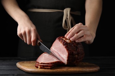 Woman cutting ham on wooden board at table, closeup