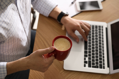 Photo of Man with cup of coffee and laptop at workplace, closeup