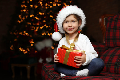 Photo of Cute little child with Christmas gift sitting in armchair at home