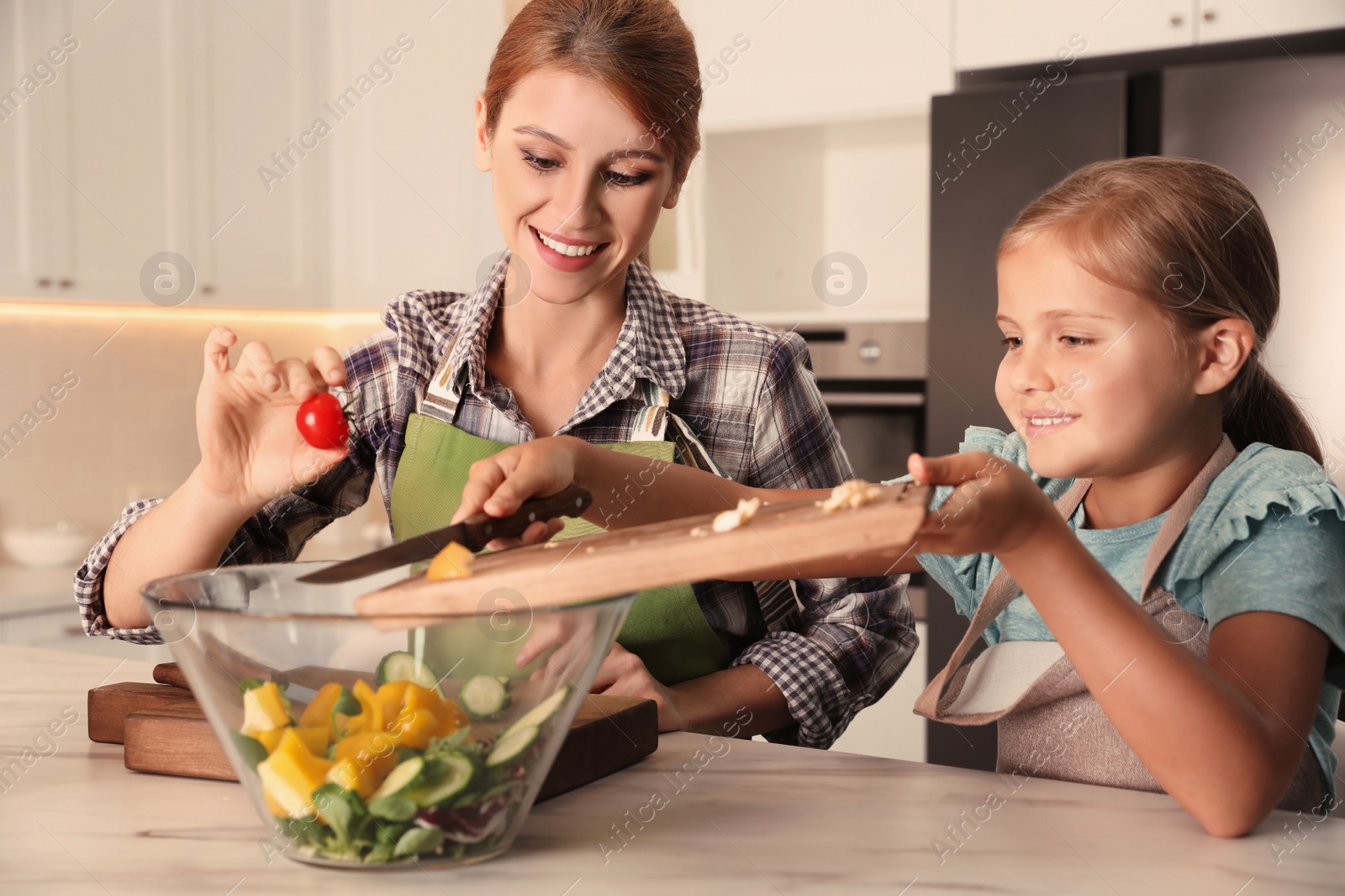 Photo of Mother and daughter cooking salad together in kitchen