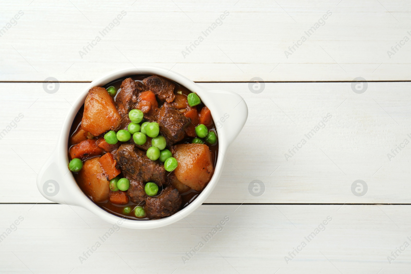 Photo of Delicious beef stew with carrots, peas and potatoes on white wooden table, top view. Space for text