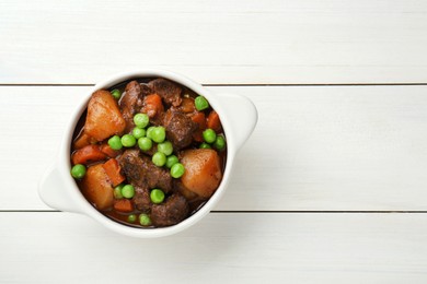 Delicious beef stew with carrots, peas and potatoes on white wooden table, top view. Space for text