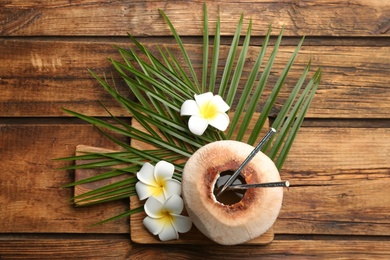 Photo of Fresh coconut with drinking straws and flowers on wooden table, flat lay
