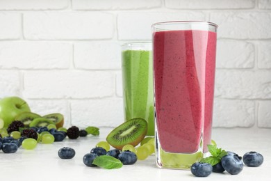 Photo of Fresh colorful fruit smoothies and ingredients on table against white brick wall. Space for text