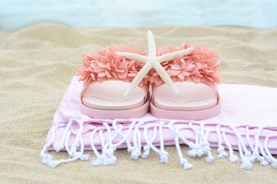 Photo of Blanket with stylish slippers and starfish on sand outdoors, closeup. Beach accessories