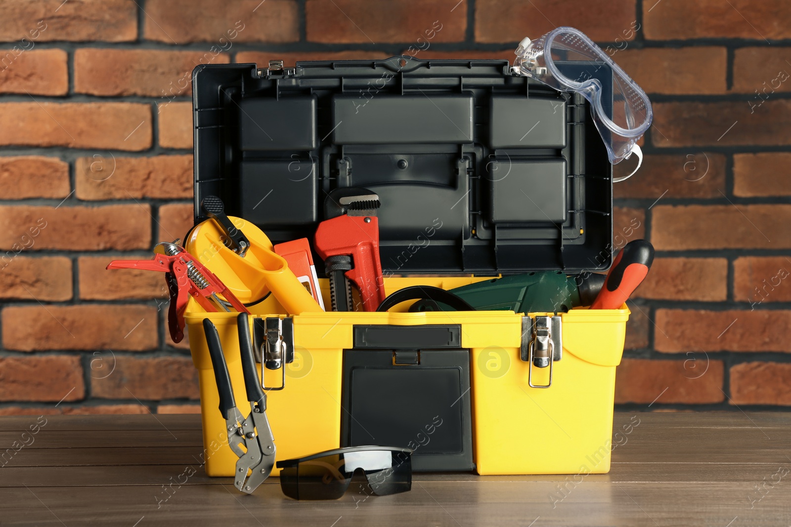 Photo of Box with different tools for repair on wooden table near brick wall