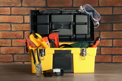 Photo of Box with different tools for repair on wooden table near brick wall